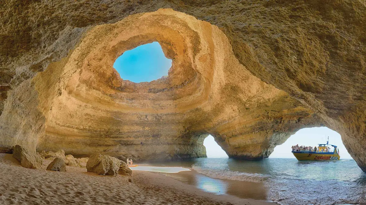 Jet boat cruising the Algarve coastline toward the Benagil sea cave with dolphins surfacing offshore near Albufeira, Portugal