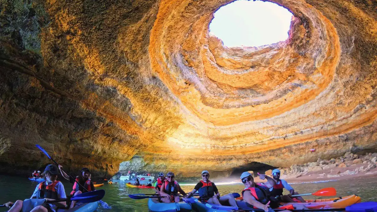 Kayakers on the sand inside the Benagil sea cave under its circular skylight, Praia da Marinha, Algarve, Portugal